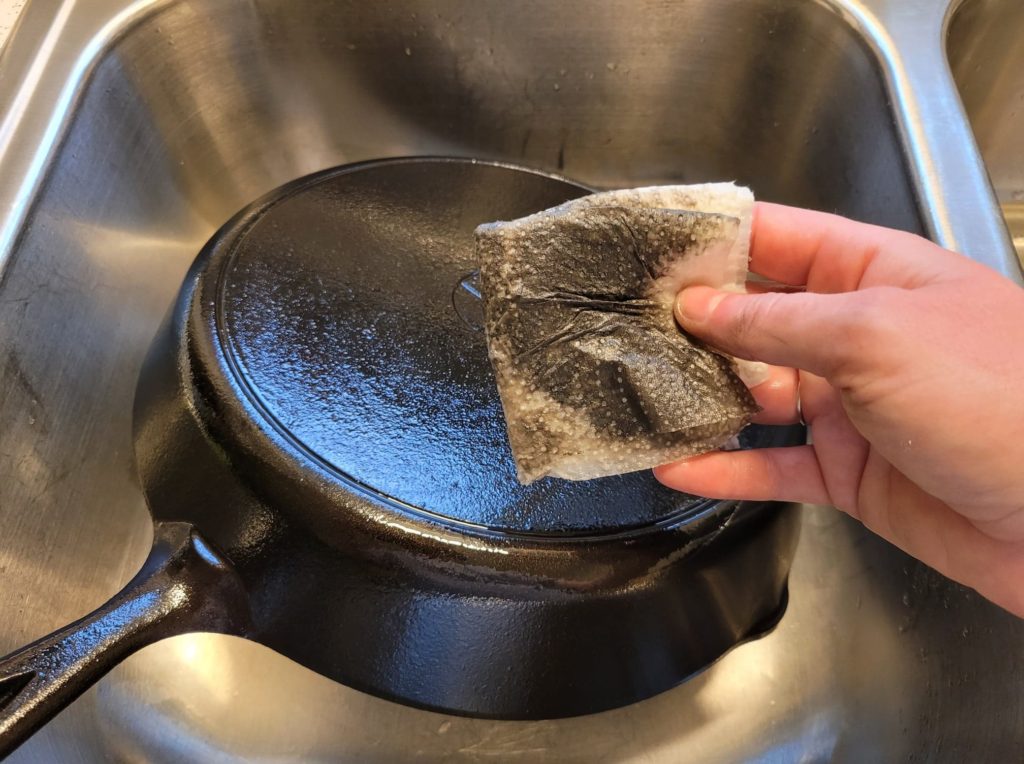 A dirty paper towel with black soot residue on it after wiping down a cast iron pan with vegetable oil 