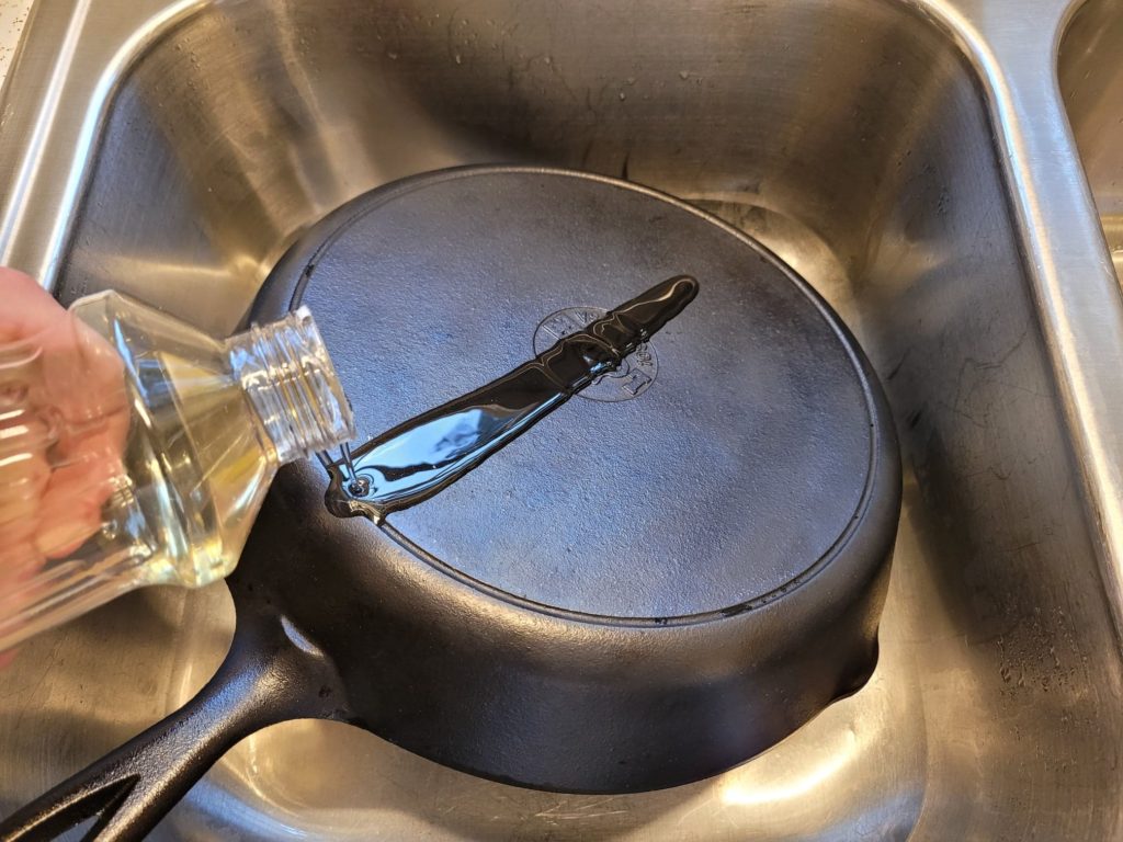 Pouring vegetable oil onto a dirty cast iron skillet in the sink