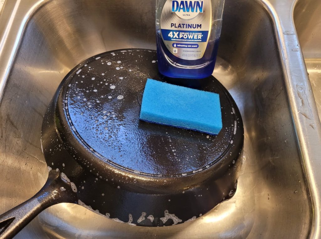 Washing a cast iron skillet with dish soap and a sponge