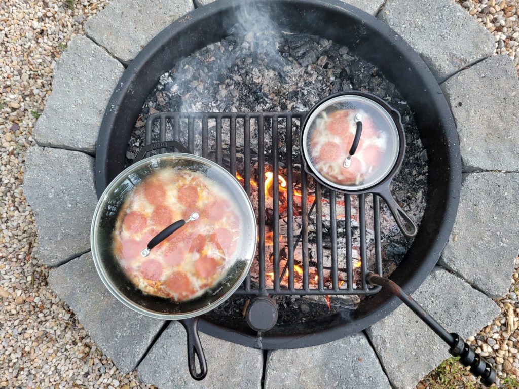 campfire pizzas cooking in cast iron skillets with lids on