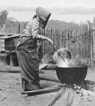 Historic photo of a woman making soap outdoors in a cauldron over an open fire.