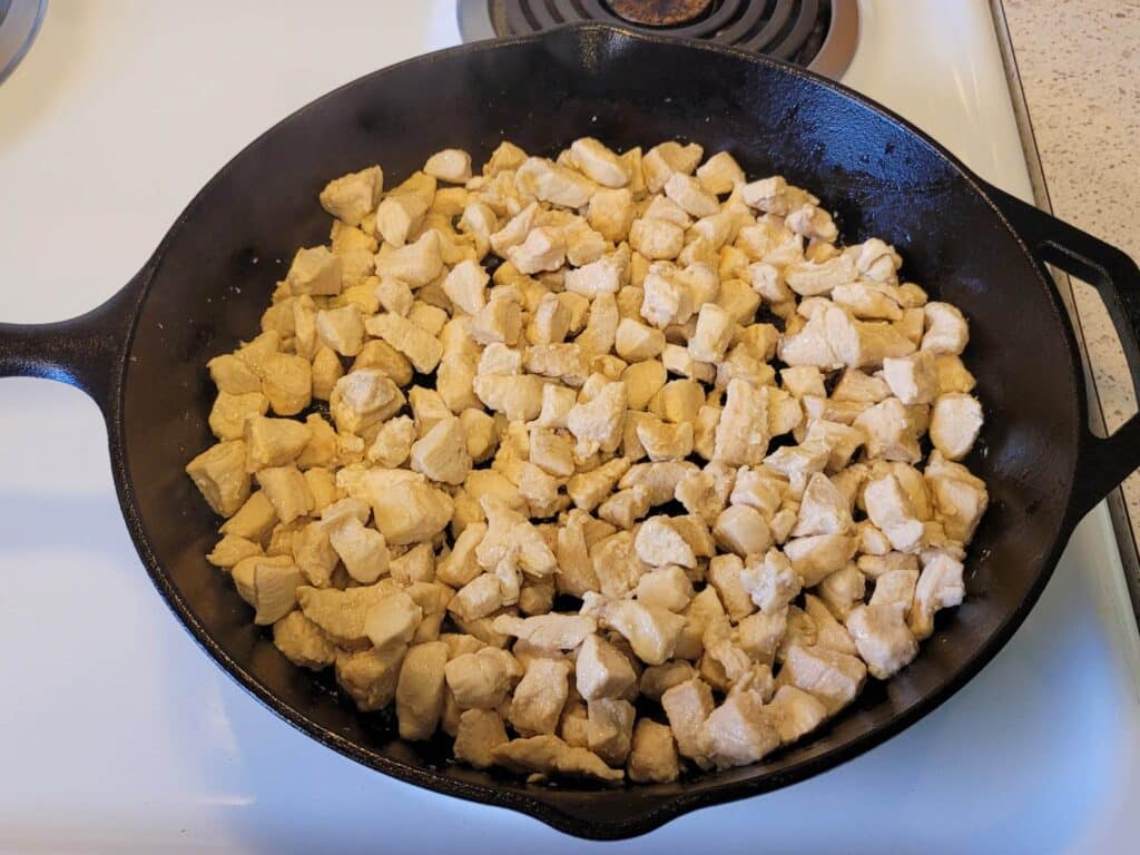 cooking cubed chicken breast in a cast iron skillet on the stovetop