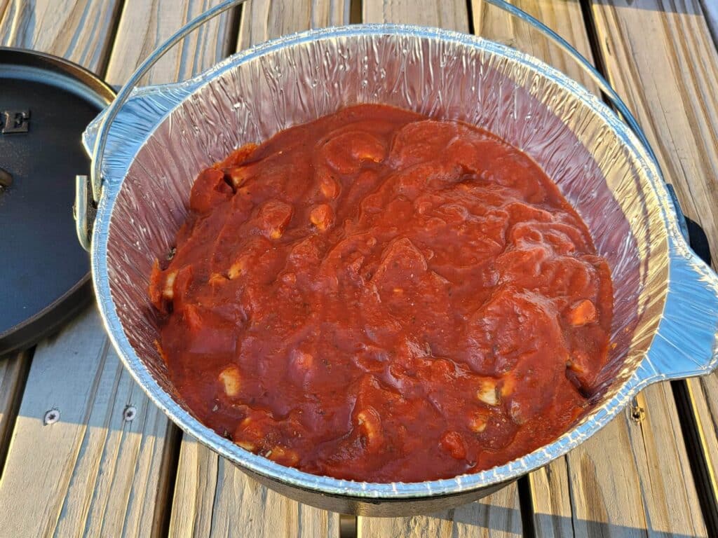 Covering chicken with pizza sauce in dutch oven