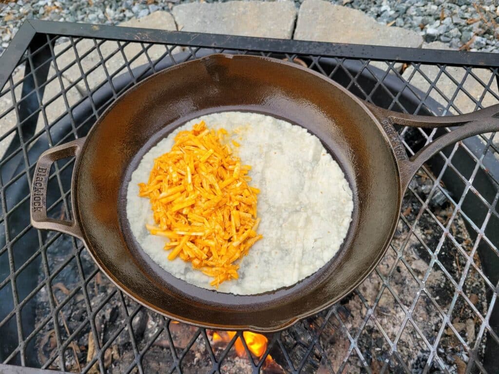 preparing buffalo chicken quesadillas in a cast iron skillet over the campfire