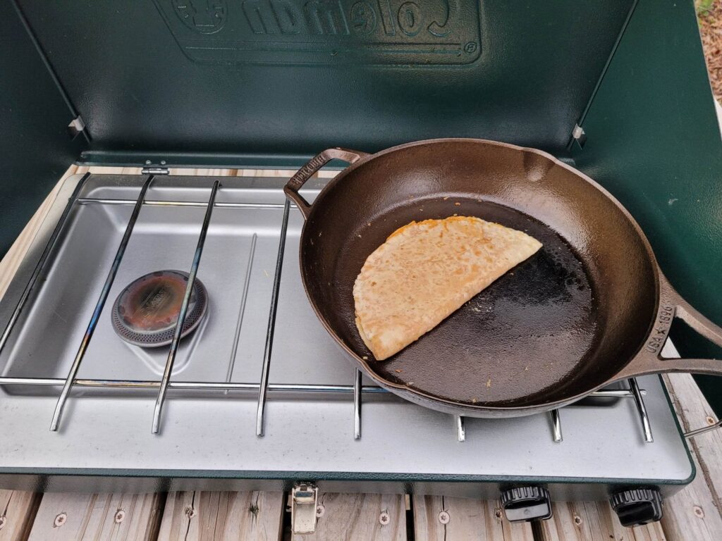 buffalo chicken quesadilla cooking in cast iron skillet on a camping stove