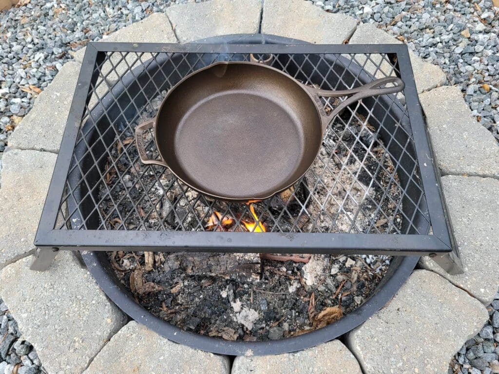 Preheating cast iron skillet on a cooking grate over the campfire