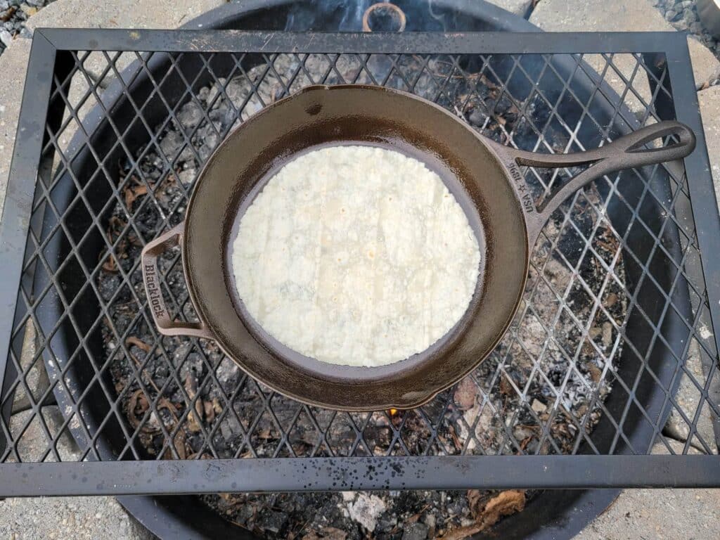 heating a tortilla in a cast iron skillet over the campfire