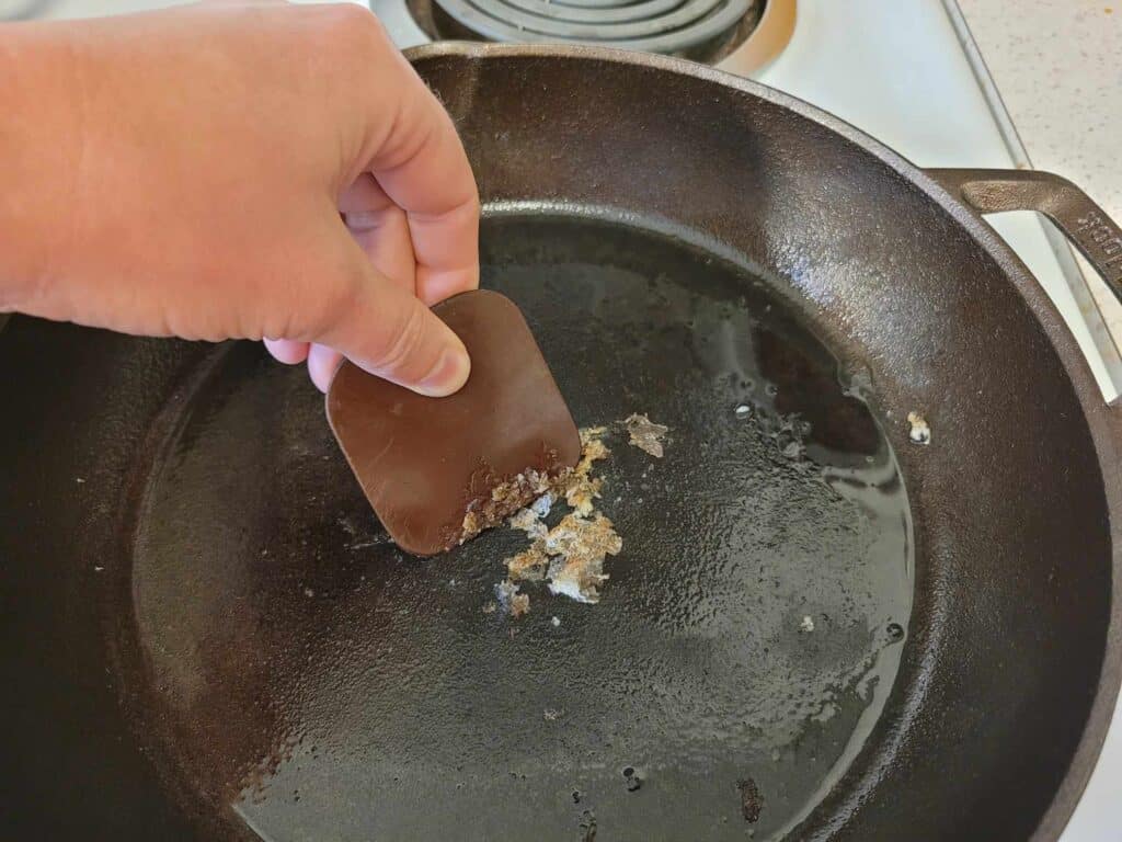 removing stuck food from a cast iron skillet with a plastic scraper