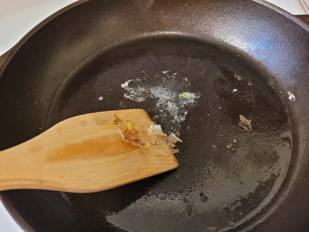 removing stuck food from a cast iron skillet with a wooden spatula